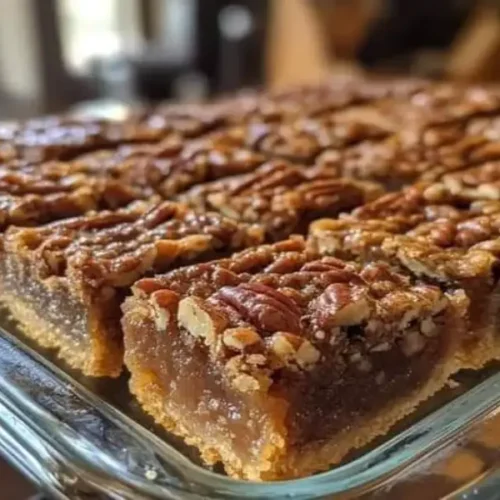 Pecan pie bars in a glass baking dish with gooey caramel pecan filling, whole pecans, and buttery shortbread crust